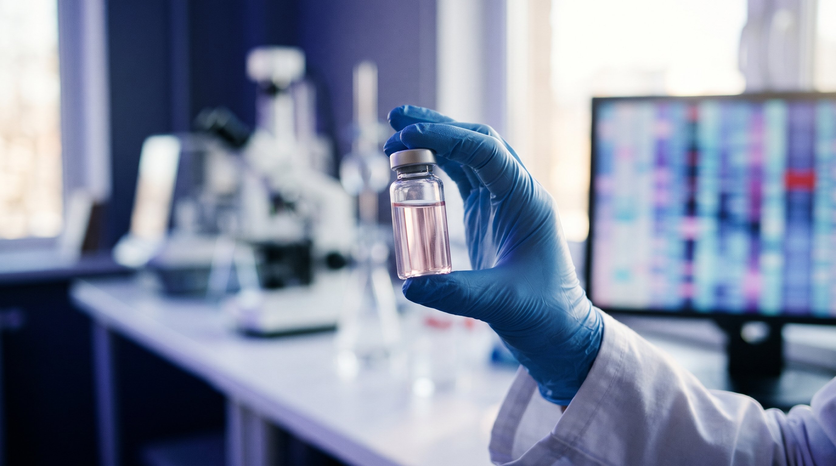 Een hand in een blauwe handschoen houdt een klein glazen flesje met lichtroze vloeistof omhoog in een lab, met op de achtergrond een wazig scherm vol gekleurde banen van een genetische analyse.
